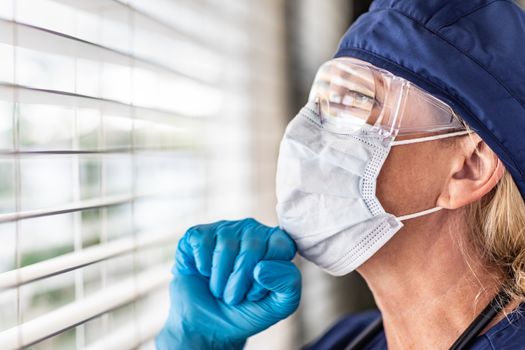 Female Doctor or Nurse On Break At Window Wearing Medical Face Mask and Goggles.