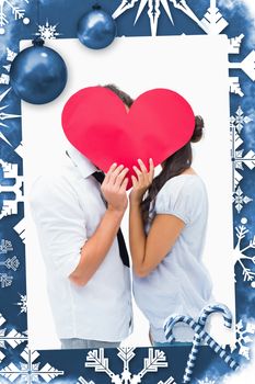 Couple covering their kiss with a heart against christmas frame