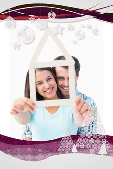 Happy young couple with house shape against christmas frame
