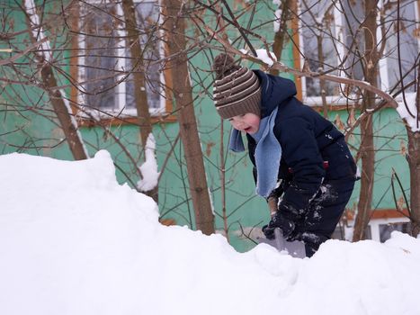 A boy in a knitted hat and with a knitted scarf in winter plays in the snow.