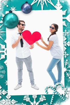 Hipster couple smiling at camera holding a heart against christmas frame