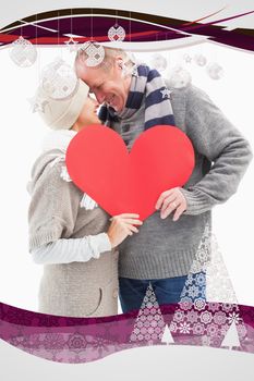 Happy mature couple in winter clothes holding red heart against christmas frame