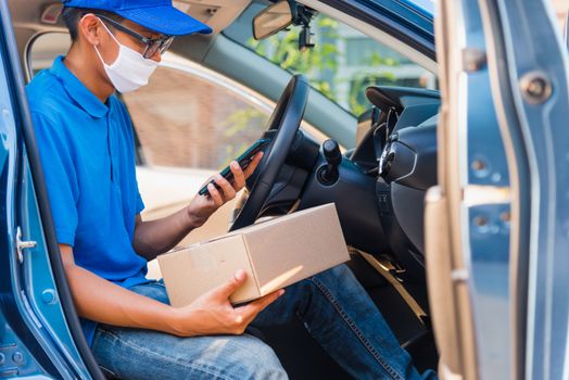 Asian delivery man courier online holding deliveries out boxes in car and using mobile phone contact the customer he protective face mask service under curfew quarantine pandemic coronavirus COVID-19