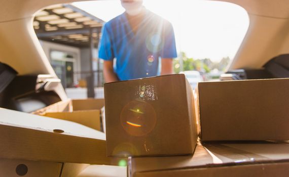 Asian delivery man courier moving deliveries out boxes in back car he protective face mask, service customer on front house under curfew quarantine pandemic coronavirus COVID-19, in car trunk view