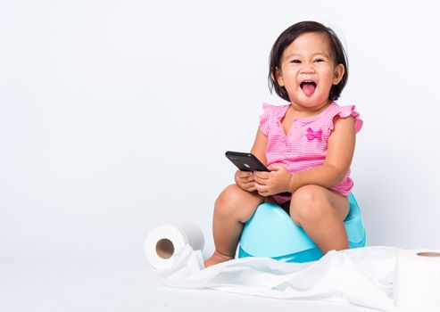 Asian little cute baby child girl education training to sitting on blue chamber pot or potty and play smart mobile phone with toilet paper rolls, studio shot isolated on white background, wc toilet