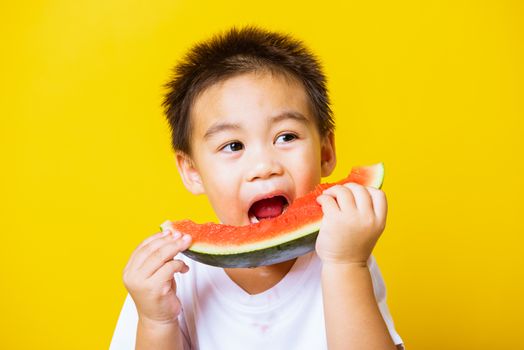 Happy portrait Asian child or kid cute little boy attractive laugh smile playing holds cut watermelon fresh for eating, studio shot isolated on yellow background, healthy food and summer concept