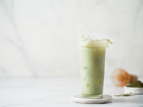 Homemade iced matcha latte with splashes on white marble background. Copy space for text or design