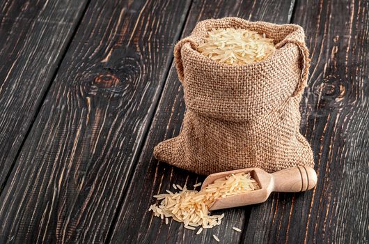 Bag with long rice and spoon stands on wooden background
