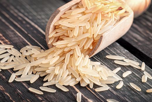 Long rice in wooden scoop closeup on dark table
