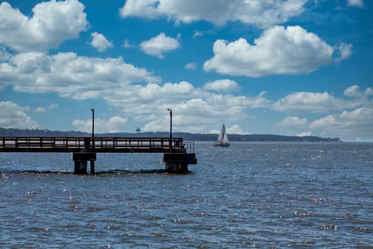 A white sailboat in blue bay beyond a dark wooden pier