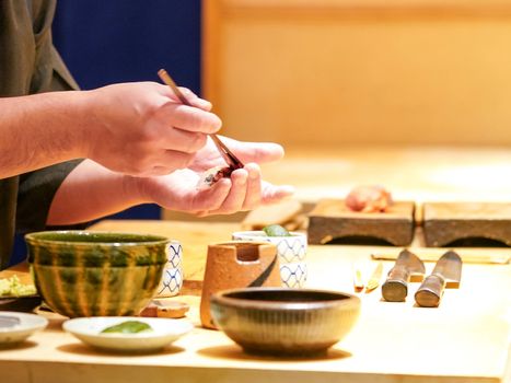 The chef is brushing shoyu sauce onto the raw fish. Enjoy Omakase experience at Japanese Sushi Restaurant.