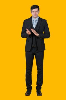 A young businessman in a gray shirt and black suit is clapping hand and starts a successful business project. The concept of business relations Portrait on a yellow background with studio lights