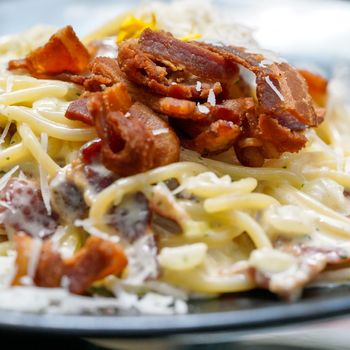 Close up Spaghetti, a delicious pasta served on black plate. Carbonara made with egg, hard cheese, guanciale, bacon and black pepper. Food Background.