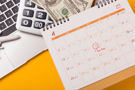 April of the year is Tax Day, Top view flat lay closeup calculator, laptop computer, calendar, and Dollar money, on yellow background business finance budget concept with copy space for text