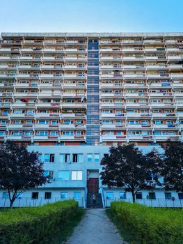 Symmetrical look to residential building with small park in front of and walking woman in center