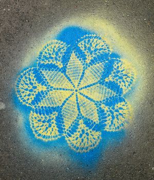 Lace pattern sprayed on pavement brick with blue and yellow spray