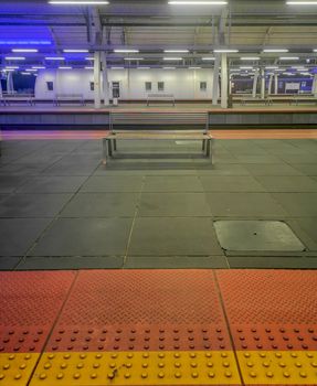 Metal bench on train station with colorful lights and red, yellow and gray pavement