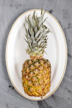 White Plate with Ripe Whole Pineapple on Grey Concrete Background