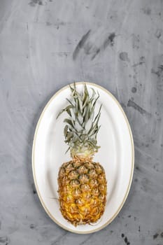 White Plate with Ripe Whole Pineapple on Grey Concrete Background. Copyspace.