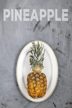 White Plate with Ripe Whole Pineapple on Grey Concrete Background. Word Pineapple