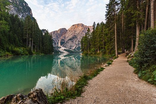 Dirt path runs along Lake Braies under a cloudy sky, in the background the Croda del Becco in Trentino Alto Adige