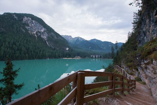 Dirt path to staircase runs along the Braies Lake under a cloudy sky, Trentino Alto Adige
