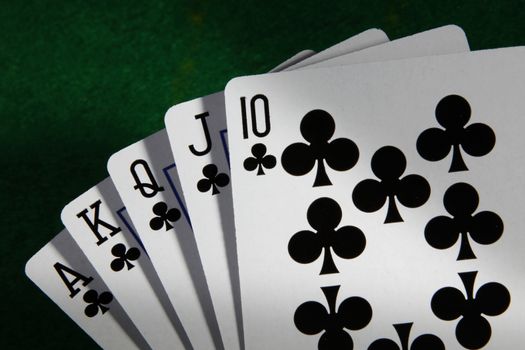 A Royal Flush in Clubs highest poker hand with green card table background and moody light