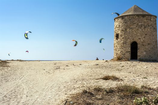 Agios Ioannis beach in Lefkas island Greece. Colorful power kites span across the sky from kite-surfers. Agios Ioannis is home to some old windmills.