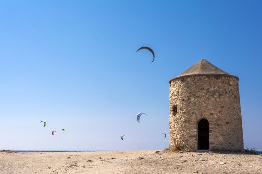 Agios Ioannis beach in Lefkas island Greece. Colorful power kites span across the sky from kite-surfers. Agios Ioannis is home to some old windmills.