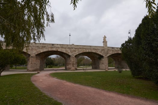 Columns and arches of stone bridge, path between vegetation, cloudy sky