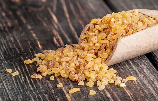 Bulgur in wooden scoop closeup on dark background