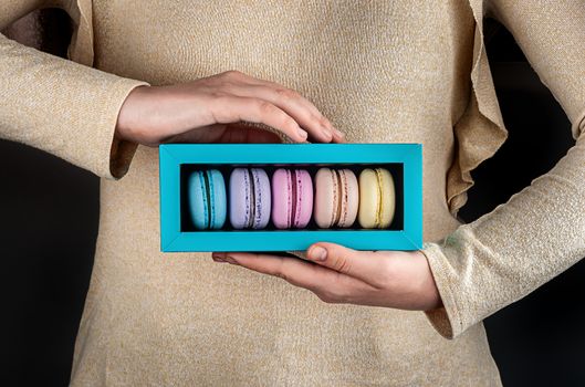 Female hands holding multicolored macaroons in gift box