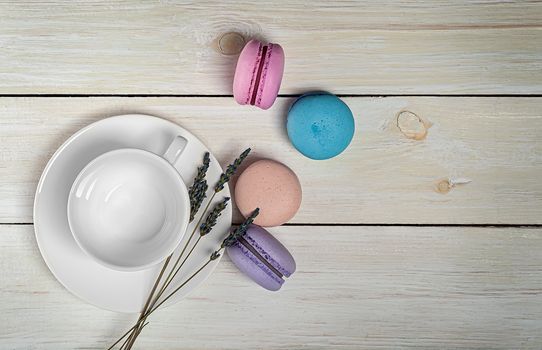 Multicolored macaroons near white coffee cup and lavender top view on wooden table