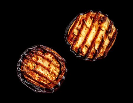 Two pieces of grilled eggplant black background