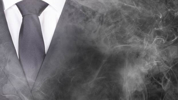 Man in a black suit and black tie, standing in smoke, close-up