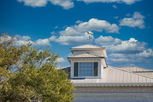 A wood cupola on a tin roof with a dolphin weathervane