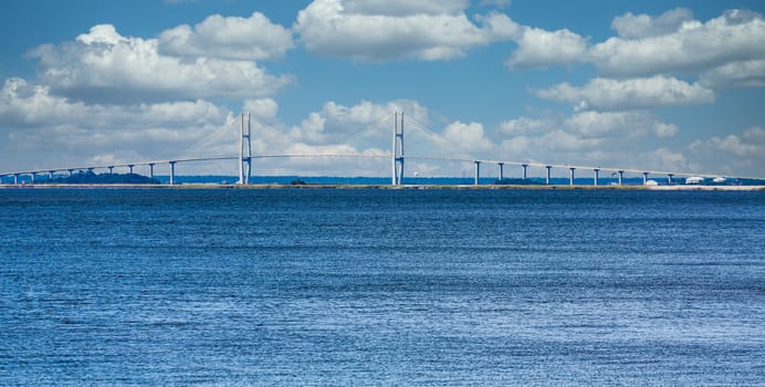 A white suspension bridge on the horizon of a blue bay