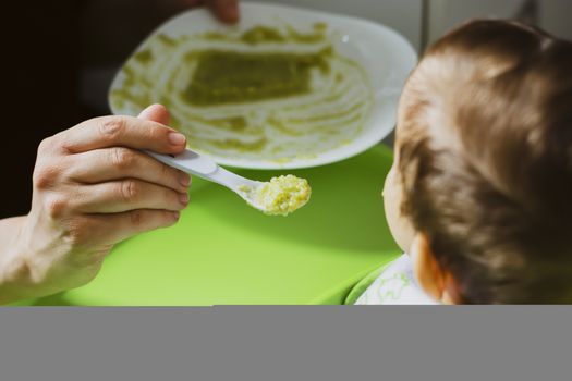 mother feeds her son with a spoon giving him a vegetable-based meal. Weaning of the newborn. Family and parenting concept. childhood