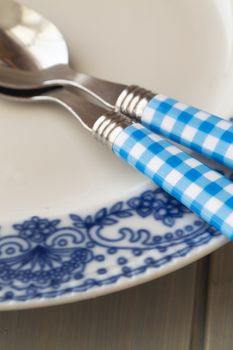 White and blue round plate with utensils on blue wooden table background, vertical image