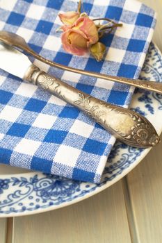 Silver fork and knife with an empty vintage plate on a blue napkin, with dry pink rose