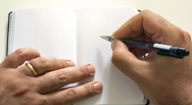 male hands holding a ballpoint pen to write on the blank pages of an open notebook. Creative moment. Inspiration.