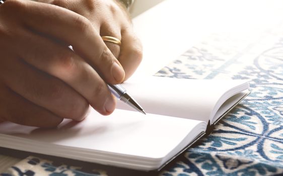 male hands holding a ballpoint pen to write on the blank pages of an open notebook. Creative moment. Inspiration.