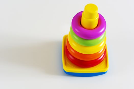 Plastic rings of various colors are stacked in a yellow plastic tower. Educational game for infants to develop their skills and creativity