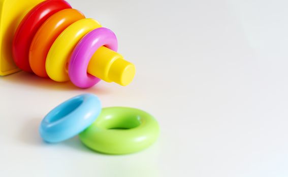 Plastic rings of various colors are stacked in a yellow plastic tower. Educational game for infants to develop their skills and creativity