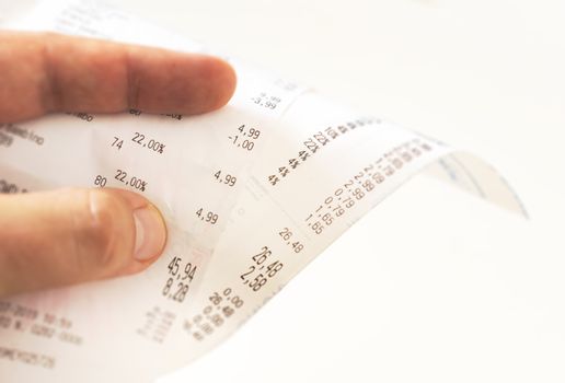 human fingers holding a paper receipt with the bill of charges and checking the total amount. Domestic finance. Tax receipt on a roll of thermal paper