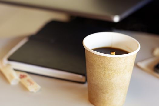 Hot coffee in a recycled paper container. Coffee break in the office. Closed book on the blurred background