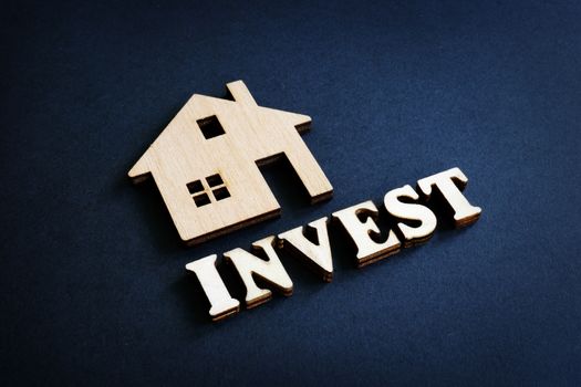 Word Invest and model of home from wood. Real Estate Investment concept.