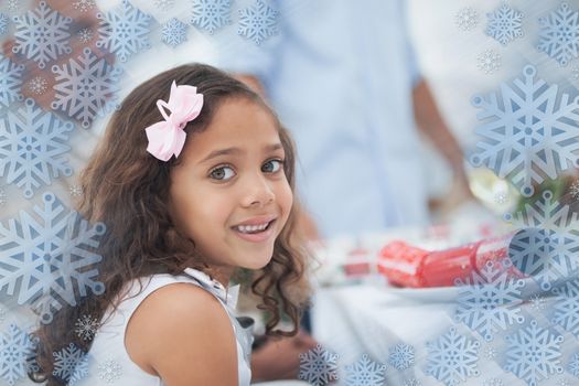 Little girl sitting at table for christmas dinner against snowflake frame