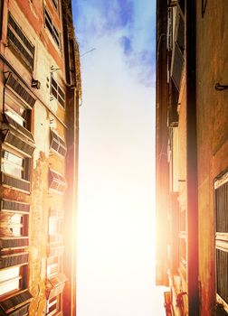 illuminated cloudy sky of the sun seen through the ancient buildings of an alley in Rome during the day. Bottom view with upward perspective.