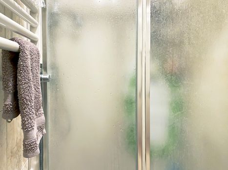 violet colored towel laid out on a white radiator near the shower enclosure with frosted glass doors and aluminum structure inside a bathroom. Interior shot